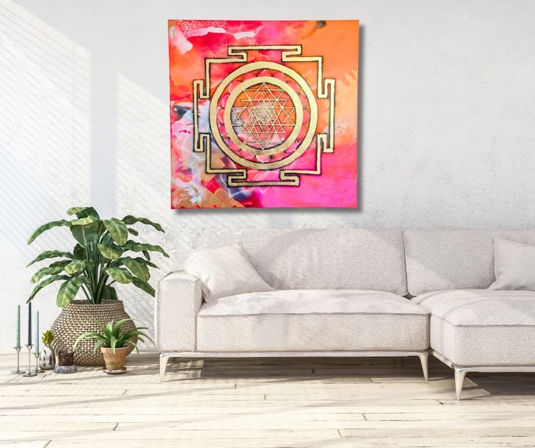 Wohnzimmer mit einer hellen Eckcouch, dekorativen Kissen, mehreren Pflanzen und einem farbenfrohen Bild mit Sri Yantra-Motiv an der Wand.